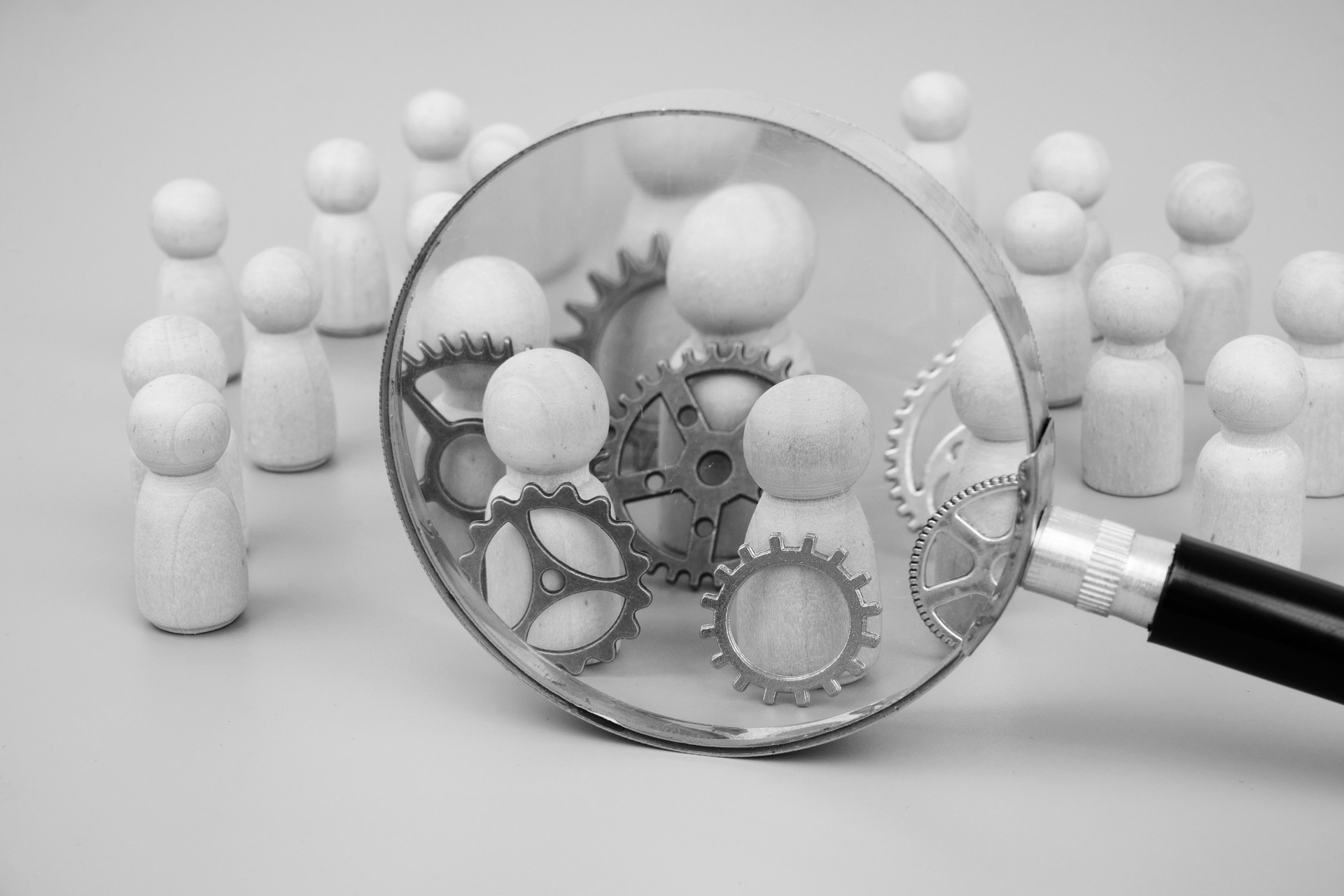 Wooden figures with different gears under magnifying glass on gray background.